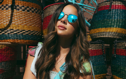Woman wearing sunglasses with reflective blue lenses in front of colorful woven baskets.